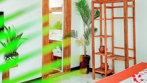 Una habitación con una cama, un estante de madera con objetos decorativos, una lámpara colgante y una puerta que da a otra habitación.