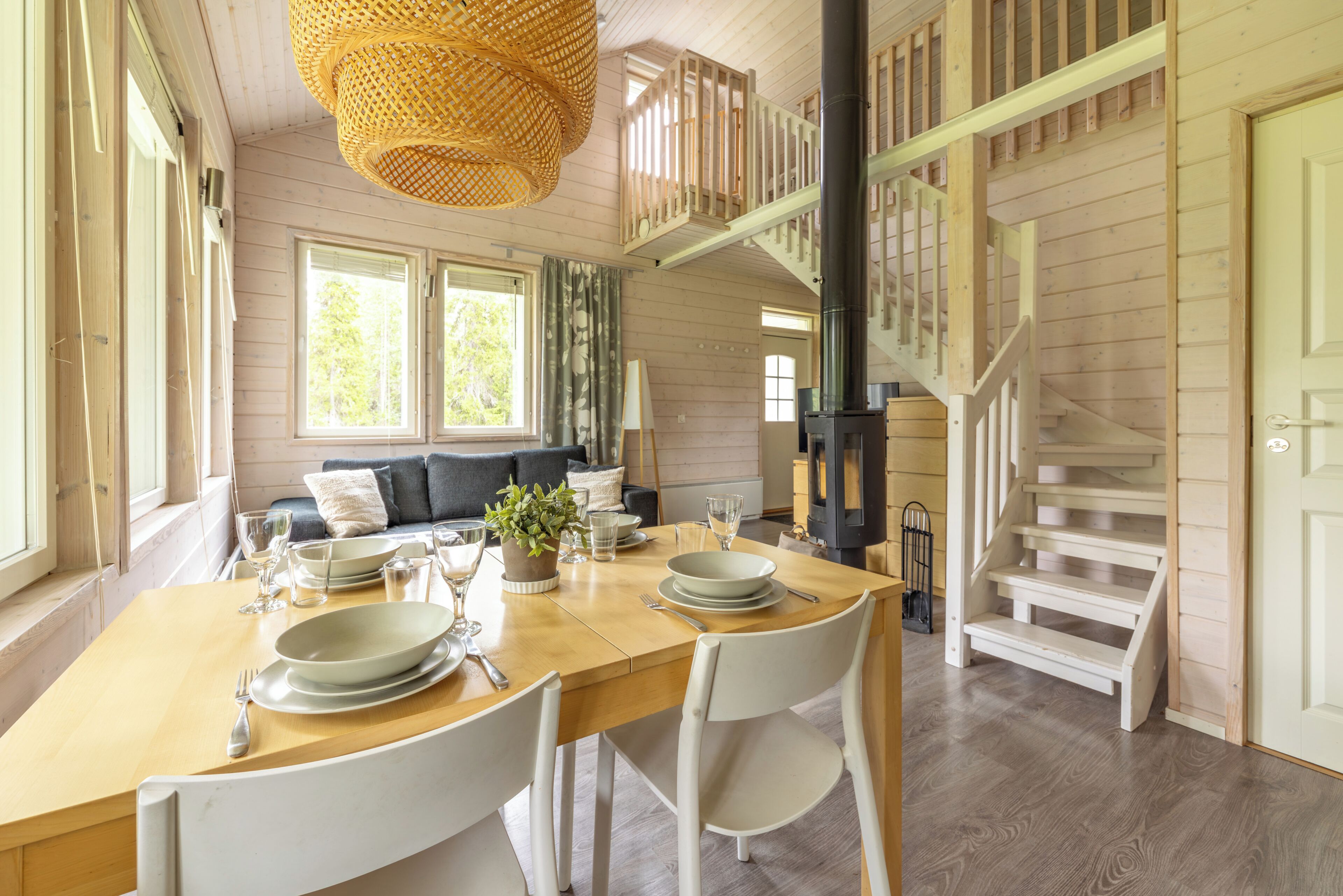 A dining area with a wooden table set for four, a staircase, and a view of the outdoors.