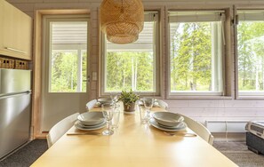 Un comedor con una mesa preparada para cuatro personas, ventanas amplias y un refrigerador.