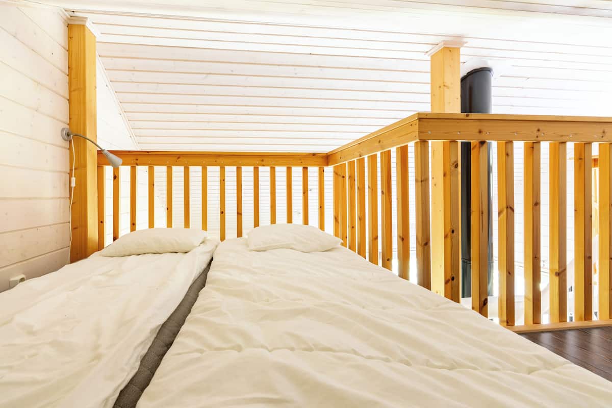 A room with a bed, wooden walls, a sloped ceiling, and a chimney.