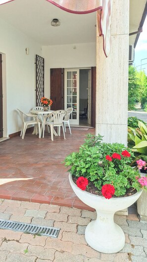 A covered patio area with a table and chairs, a potted plant with red flowers, and a door leading to an interior space. - Casa degli Orti di Venezia (Dolo)