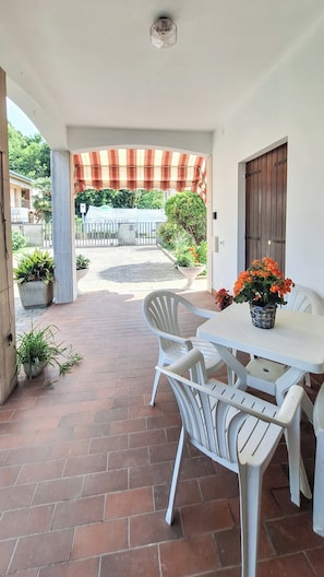 Eine überdachte Terrasse mit Tisch und Stühlen, Blumentöpfen und Blick auf die Straße.