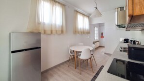 A compact kitchen with a refrigerator, a dining table with chairs, a hanging light fixture, and a microwave. - Casa degli Orti di Venezia (Dolo)