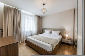 Ein modernes Hotelzimmer mit einem großen Bett, Nachttischen, einem Schreibtisch und einer Pendelleuchte.