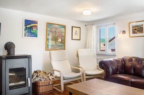 A cozy living room with a fireplace, two white chairs, a leather sofa, and artwork on the walls.