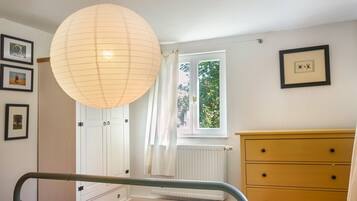 A bedroom with a bed, a dresser, a radiator, a window with curtains, and framed pictures on the wall.