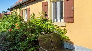 A building with a yellow exterior, a window with brown shutters, and a metal chair in front. - Apartment 'Alte Schmiede Ellrichshausen' with Wi-Fi (Satteldorf)