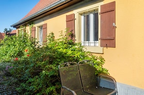 A building with a yellow exterior, a window with brown shutters, and a metal chair in front.