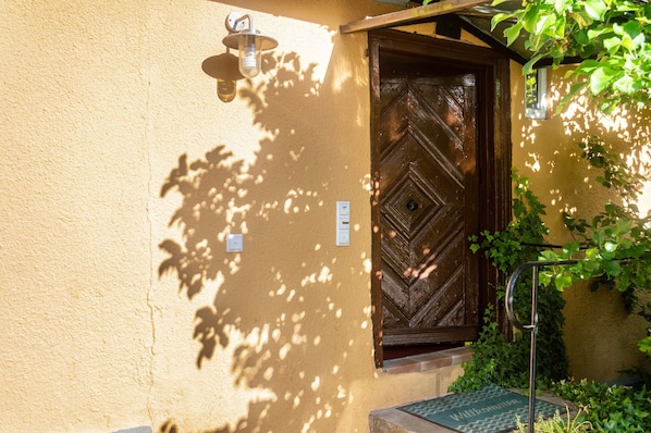 A wooden door with a diamond pattern, a wall-mounted light fixture, and a doormat with the name 'Wilhelm'.