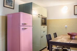 Eine kleine Küche mit einem pinken Kühlschrank, einer Mikrowelle und einem Esstisch mit Stühlen.