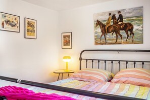 Une chambre à coucher avec un lit, un tableau représentant des cavaliers et des photos encadrées accrochées au mur.