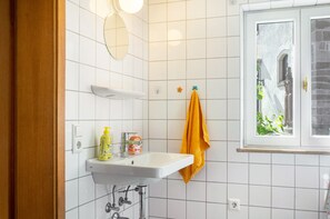 Une salle de bain avec un lavabo blanc, un miroir et une fenêtre.