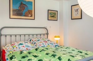 A bed with a metal frame, colorful pillows, a green blanket with animal prints, and a wall with framed artwork.