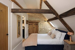 Ein Schlafzimmer mit Steinwand, Holzbalken, einem Bett mit Kissen, einem Nachttisch und einem Spiegel.