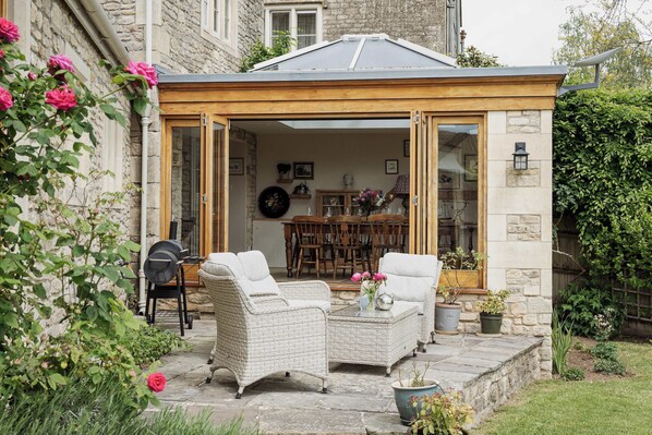 Eine gemütliche Terrasse mit Korbmöbeln, einem Grill und Blumentöpfen.