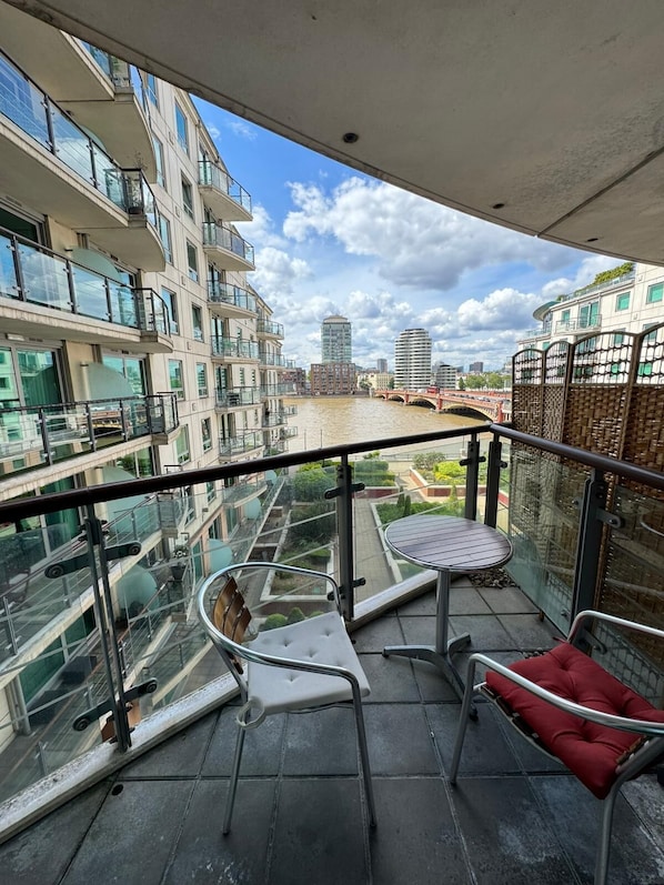 Ein Balkon mit Glasgeländer, zwei Stühle, ein Tisch und ein rotes Kissen.
