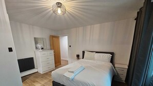 Une chambre à coucher comprenant un lit, une table de chevet, une commode et un luminaire fixé au plafond.
