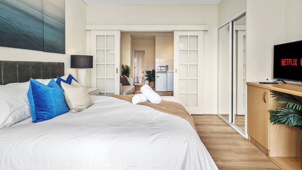 Una habitación de hotel moderna con una cama grande, televisión y vistas al área de la cocina.