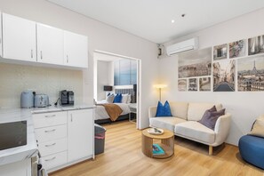 Ein kompakter Wohnraum mit Küchenzeile, einem Bett, einer Couch und einem Couchtisch.