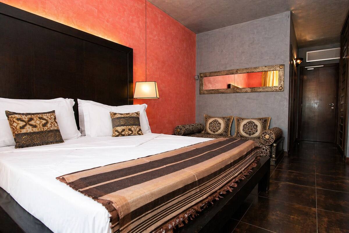 Ein Hotelzimmer mit einem großen Bett, einer Nachttischlampe, einem Spiegel und einem dunklen Holzkopfstück.