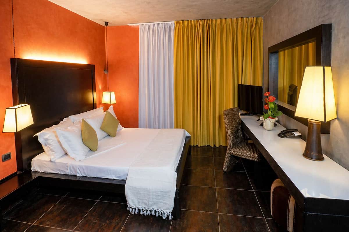 Ein Hotelzimmer mit einem Bett, Nachttischlampen, einem Schreibtisch mit Telefon und einem Spiegel.