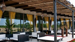 An outdoor seating area with tables and chairs, a pergola structure, and a view of the landscape. - Hotiday Otranto Baia Resort (Otranto)