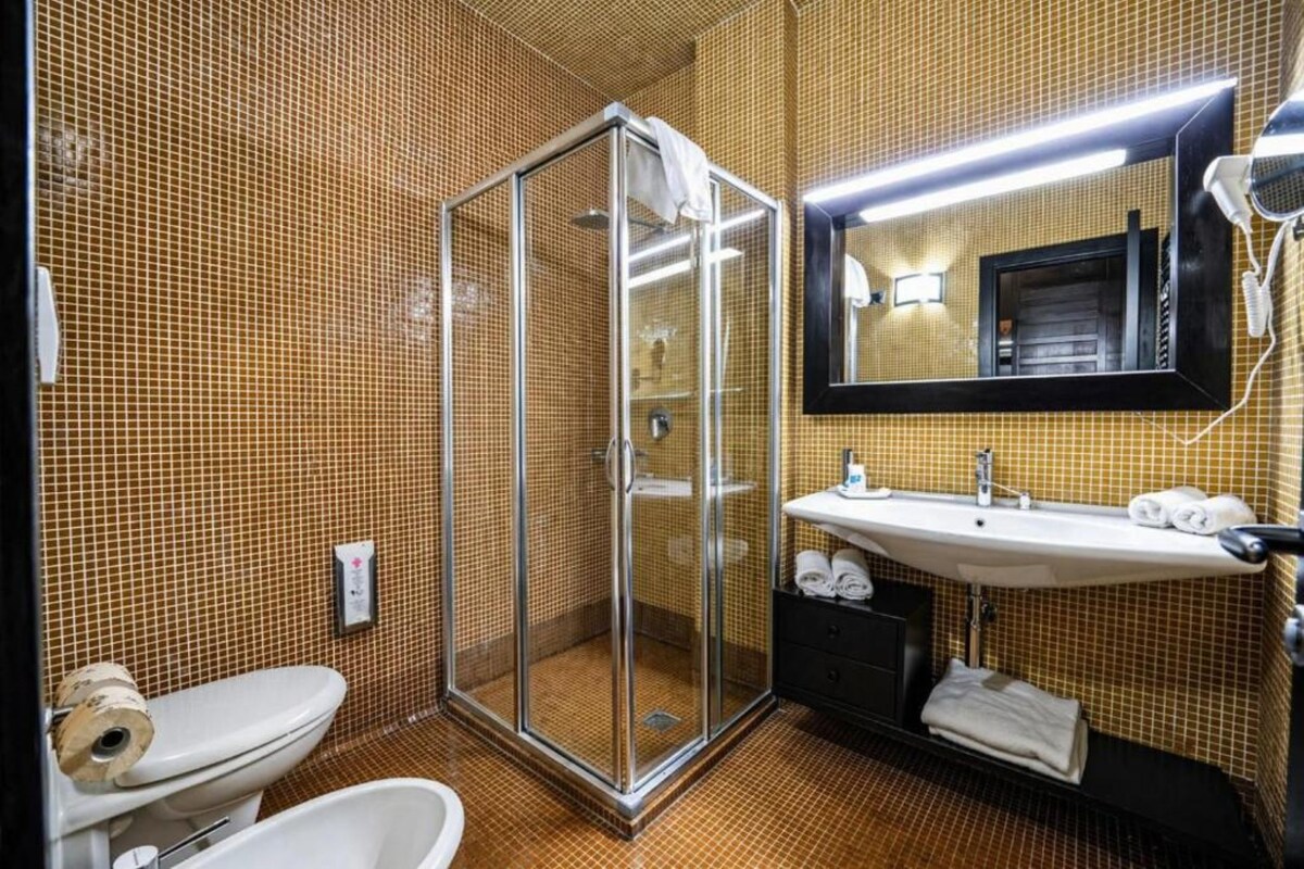 A bathroom with a glass shower enclosure, a sink with a mirror above it, and a toilet.