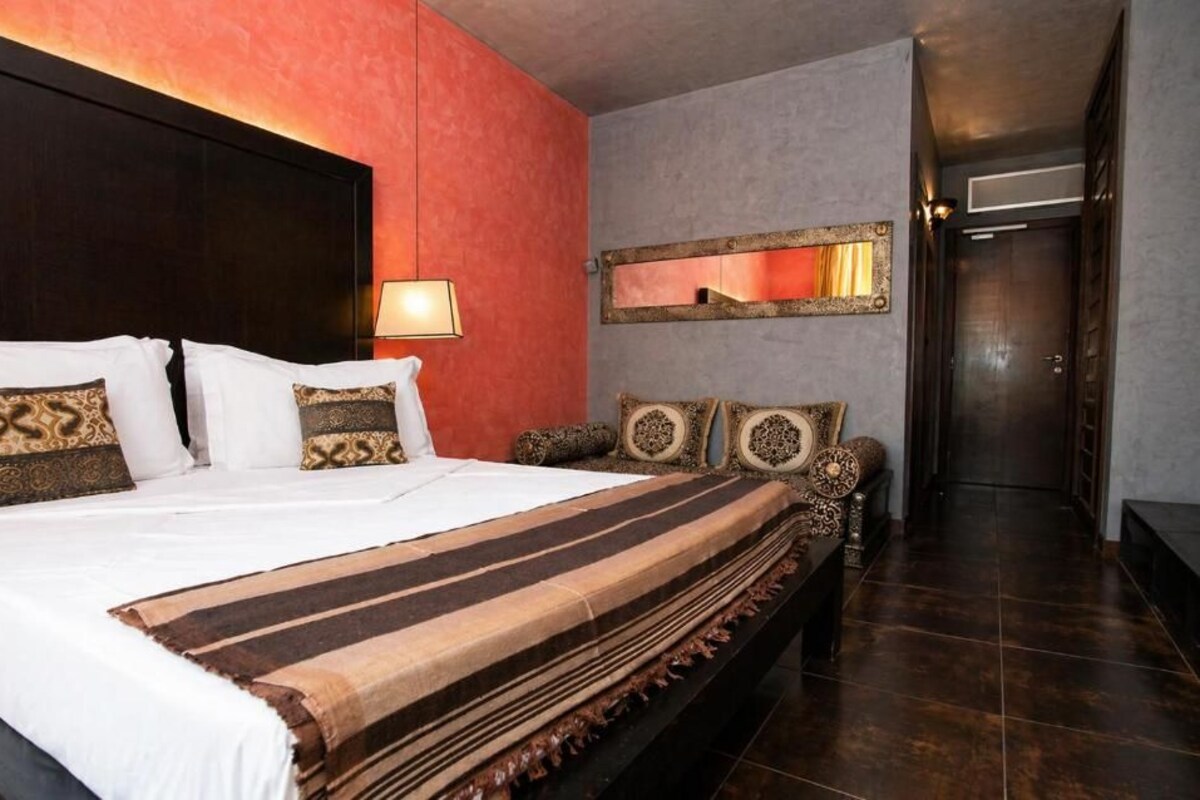 A hotel room with a large bed, a bedside table, a mirror, and a door leading to another room.