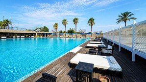 A pool with wooden deck, lounge chairs, and palm trees. - Hotiday Otranto Baia Resort (Otranto)