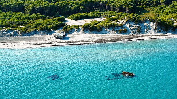 A coastal area with clear turquoise water, a boat, and a building on the shore. - Hotiday Otranto Baia Resort (Otranto)