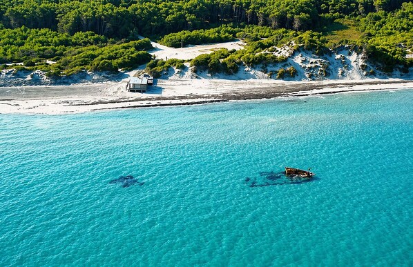 A coastal area with clear turquoise water, a boat, and a building on the shore.