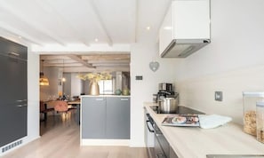 A modern kitchen with grey cabinets, a central island, and a dining area with a table and chairs. - Duinhalm - located in the heart of Nieuwpoort (Nieuwpoort)