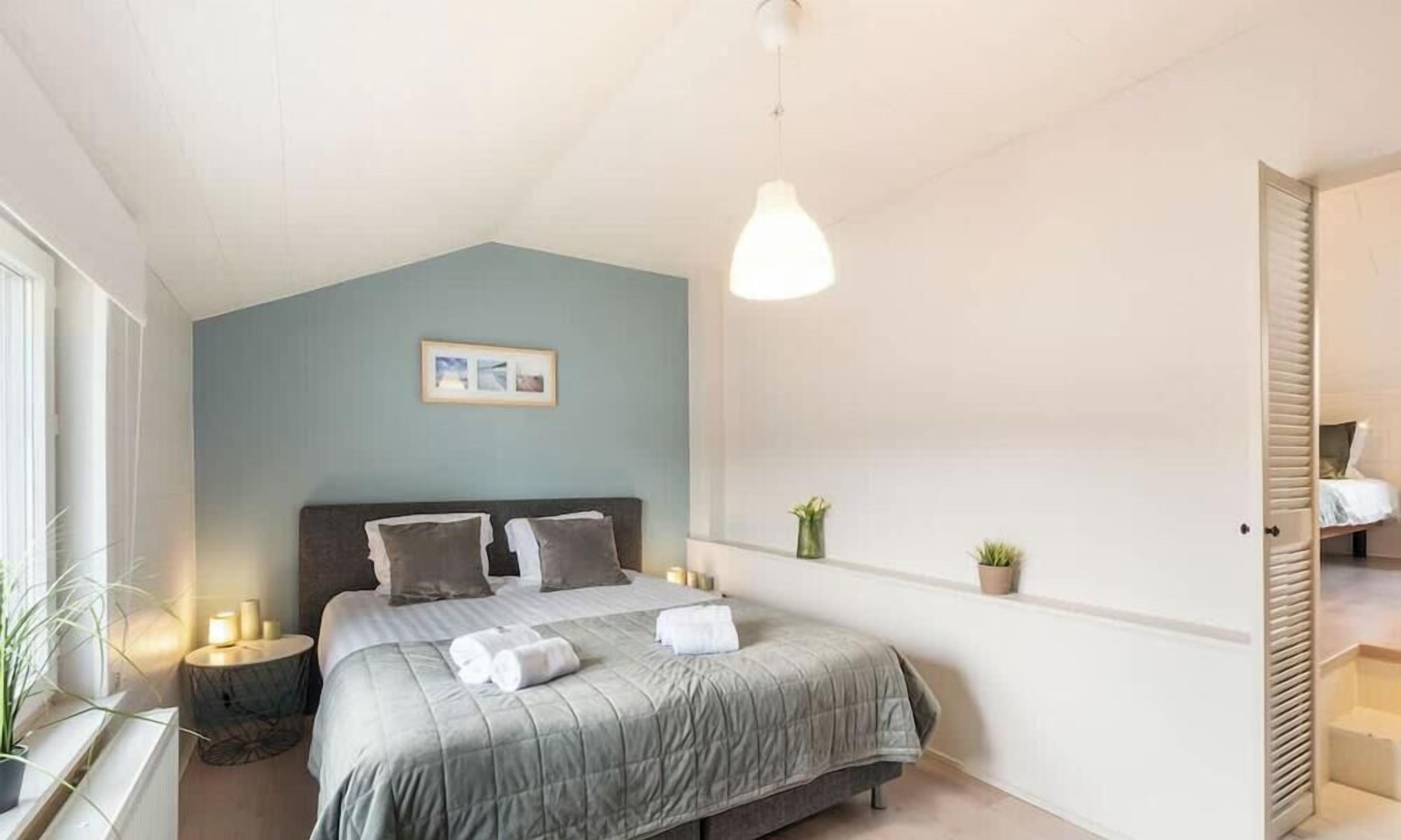 A bedroom with a bed, bedside lamps, a hanging light, a framed picture, and a potted plant.