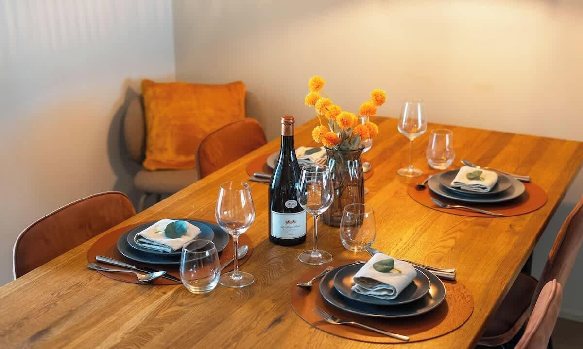 Een eettafel gedekt met borden, bestek, wijnglazen en een fles wijn.