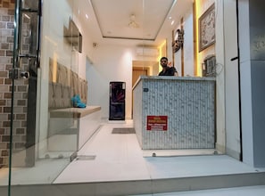 A hotel reception area with a marble reception desk, a seating area with a blue cushion, and a wall-mounted clock. - Hotel Shree Krishna Inn (Ujjain)