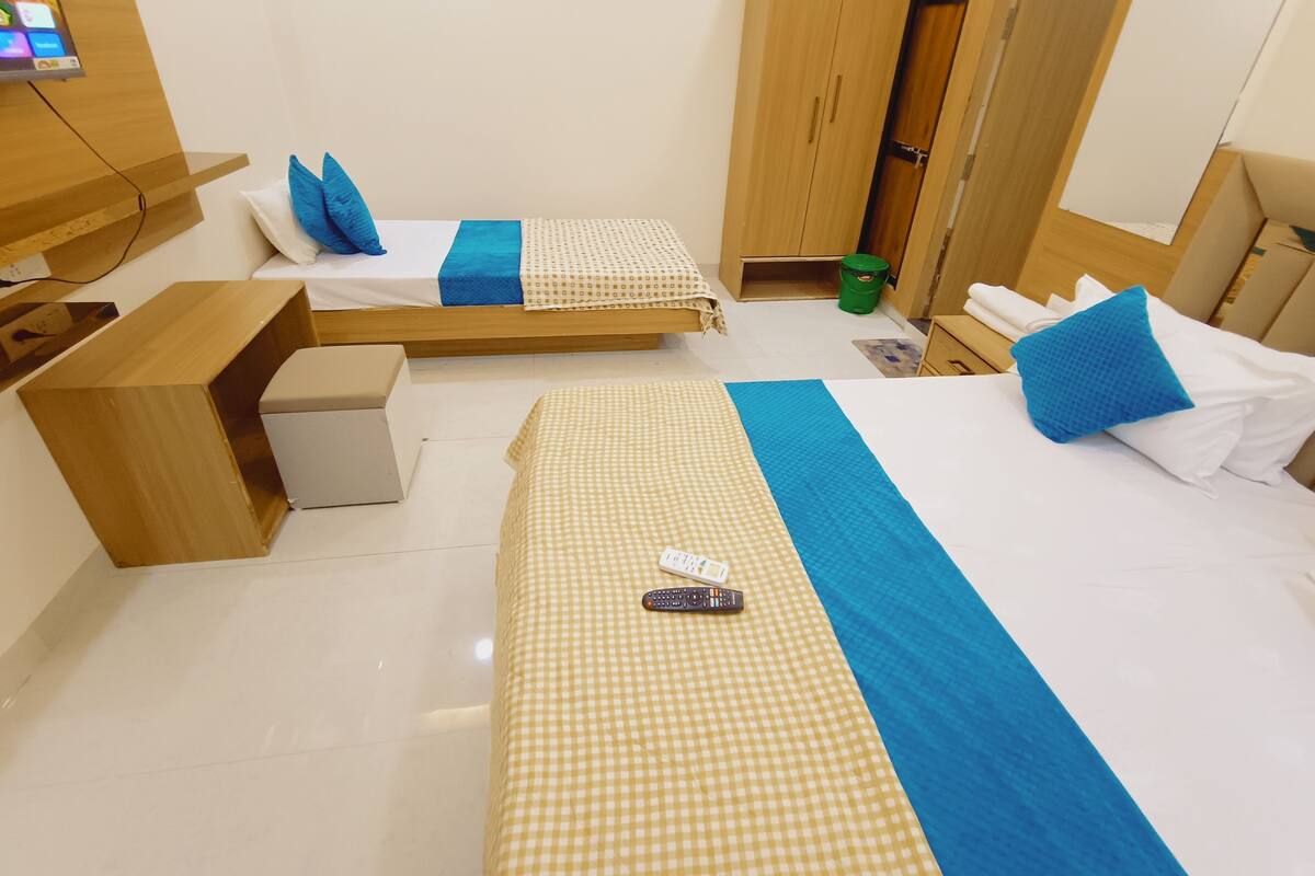Habitación de hotel con dos camas, un armario de madera, un escritorio pequeño y un televisor montado en la pared.