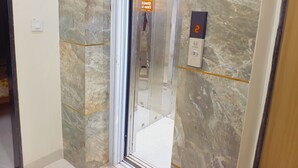 An elevator with a marble wall, a digital display showing the number 2, and a sign with emergency instructions. - Hotel Shree Krishna Inn (Ujjain)