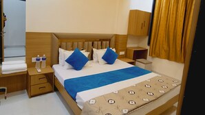 A hotel room with a wooden bed, a bedside table with a lamp, a wardrobe, and a window with curtains. - Hotel Shree Krishna Inn (Ujjain)