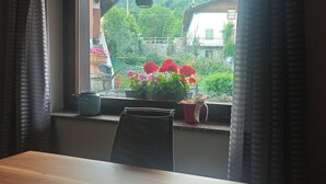 A room with a wooden table, a window with curtains, and a view of houses and greenery. - "Al Planet" Mountain Lodging: Hiking and Golf (Fiou)