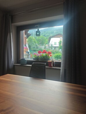 A room with a wooden table, a window with curtains, and a view of houses and greenery. - "Al Planet" Mountain Lodging: Hiking and Golf (Fiou)