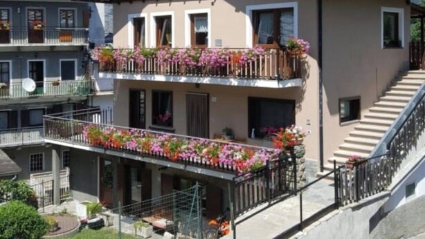 A two-story building with balconies adorned with flowers, a staircase leading to the upper floor, and a mountainous backdrop. - "Al Planet" Mountain Lodging: Hiking and Golf (Fiou)