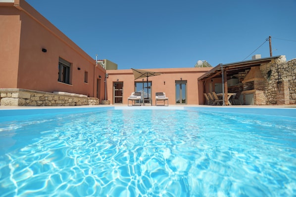 A swimming pool with lounge chairs, a stone wall, and a building with a flat roof.