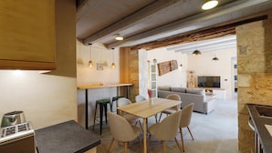Una cocina moderna con comedor, una pared de piedra y una sala de estar con sofá y televisor.