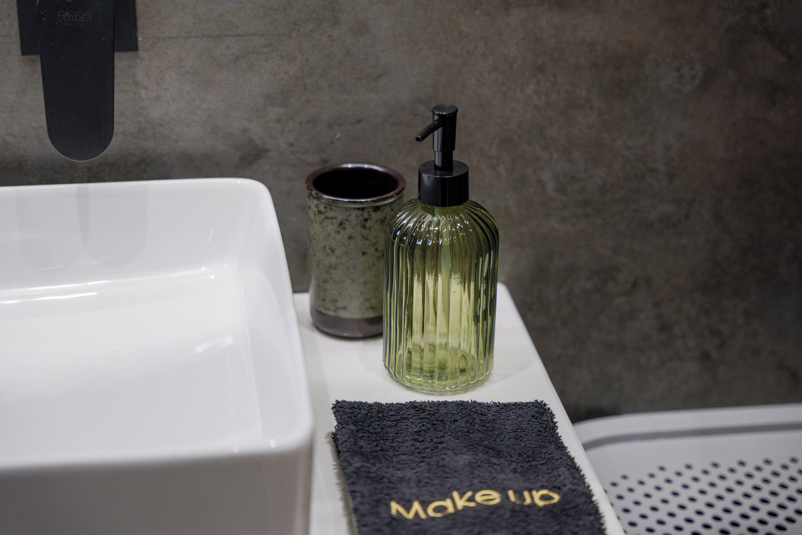 A bathroom sink, a glass bottle with a pump, a small container, and a towel with 'make up' text.