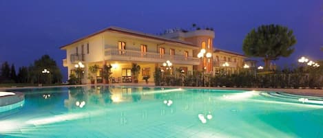 A large, multi-story hotel with a swimming pool, balconies, and outdoor lighting.