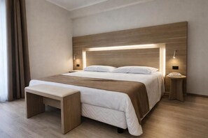 A modern hotel room with a large bed, bedside tables, a bench, and a headboard with integrated lighting. - Hotiday Corato (Corato)