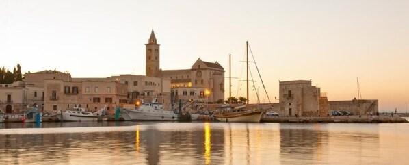 A coastal town with historic buildings, a prominent tower, and boats docked at the harbor. - Hotiday Corato (Corato)
