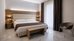 A modern hotel room with a large bed, bedside lamps, a bench, and a chair.