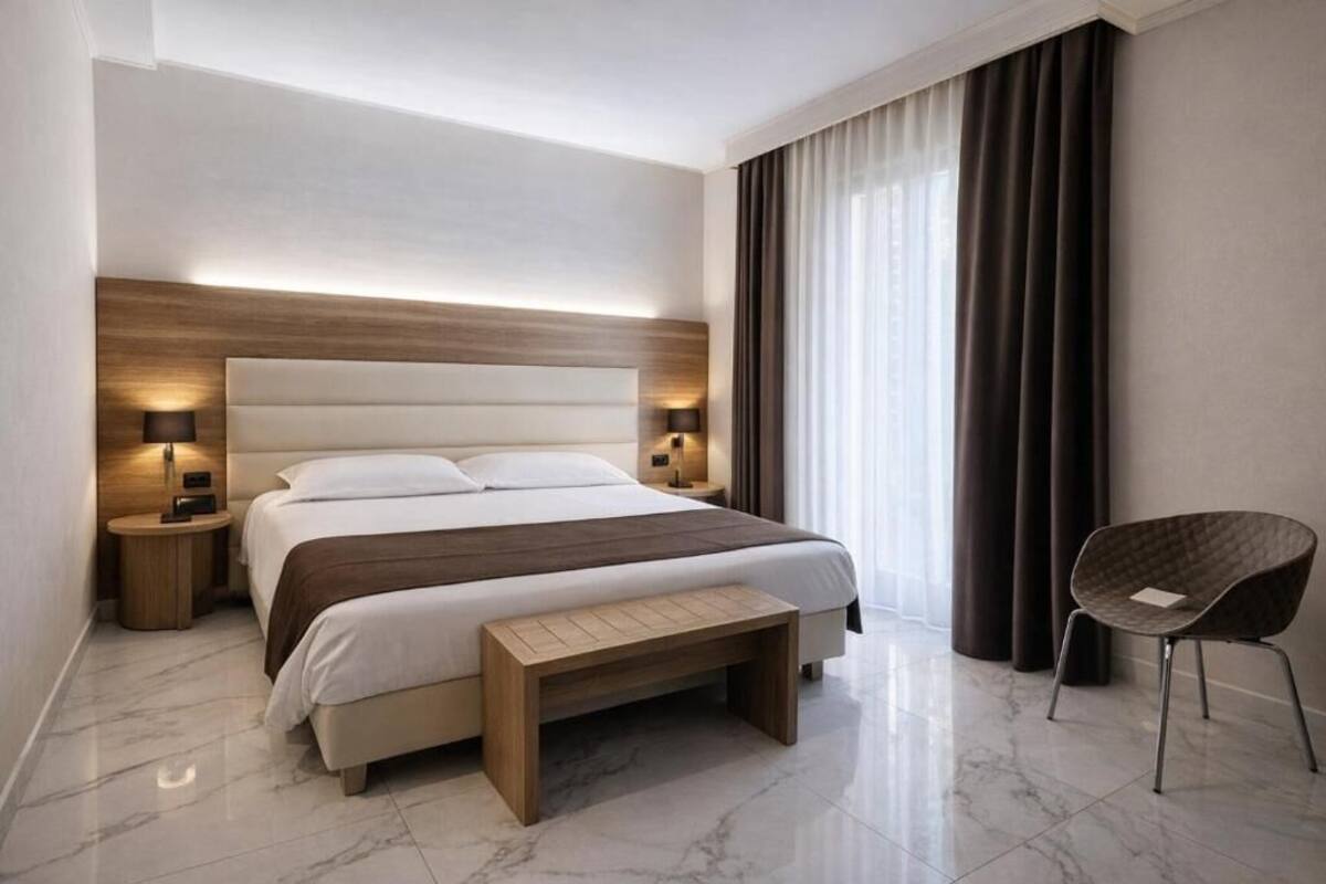 A modern hotel room with a large bed, bedside lamps, a bench, and a chair.