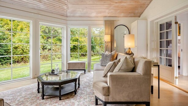 Una habitación amplia con ventanas grandes, un sofá cómodo, una mesa de centro de vidrio y una lámpara.
